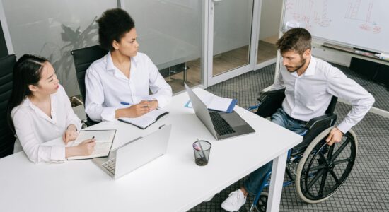 Three people sat around a desk, in an office. One person is in a wheelchair.